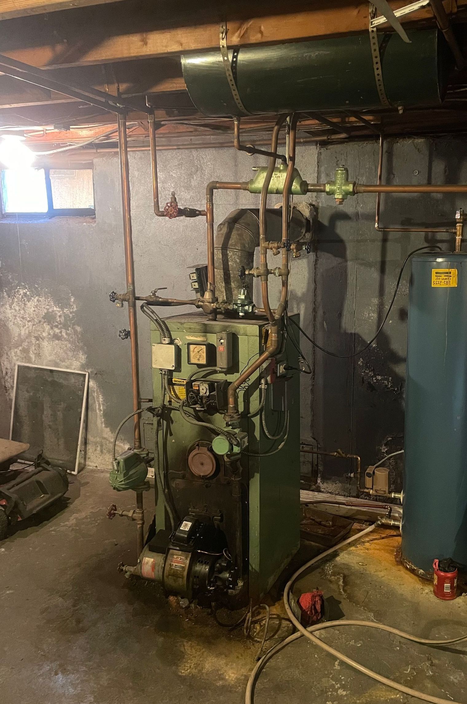 A boiler is sitting in a basement next to a water heater.