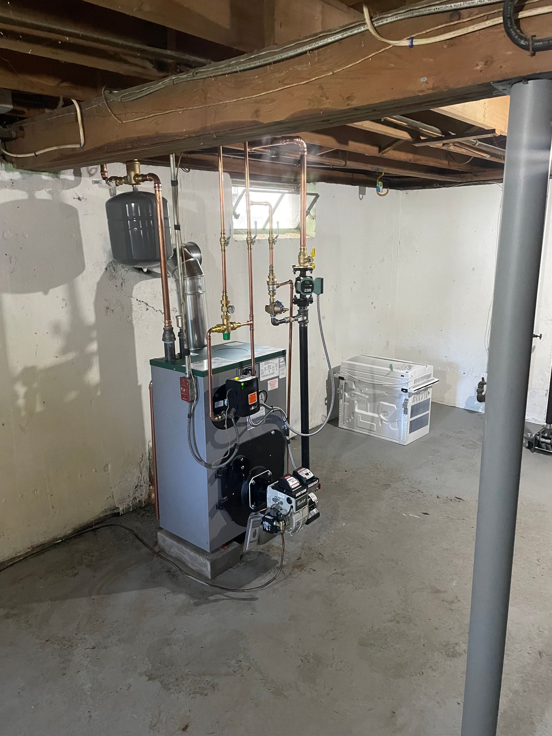 A basement with a boiler and pipes hanging from the ceiling.