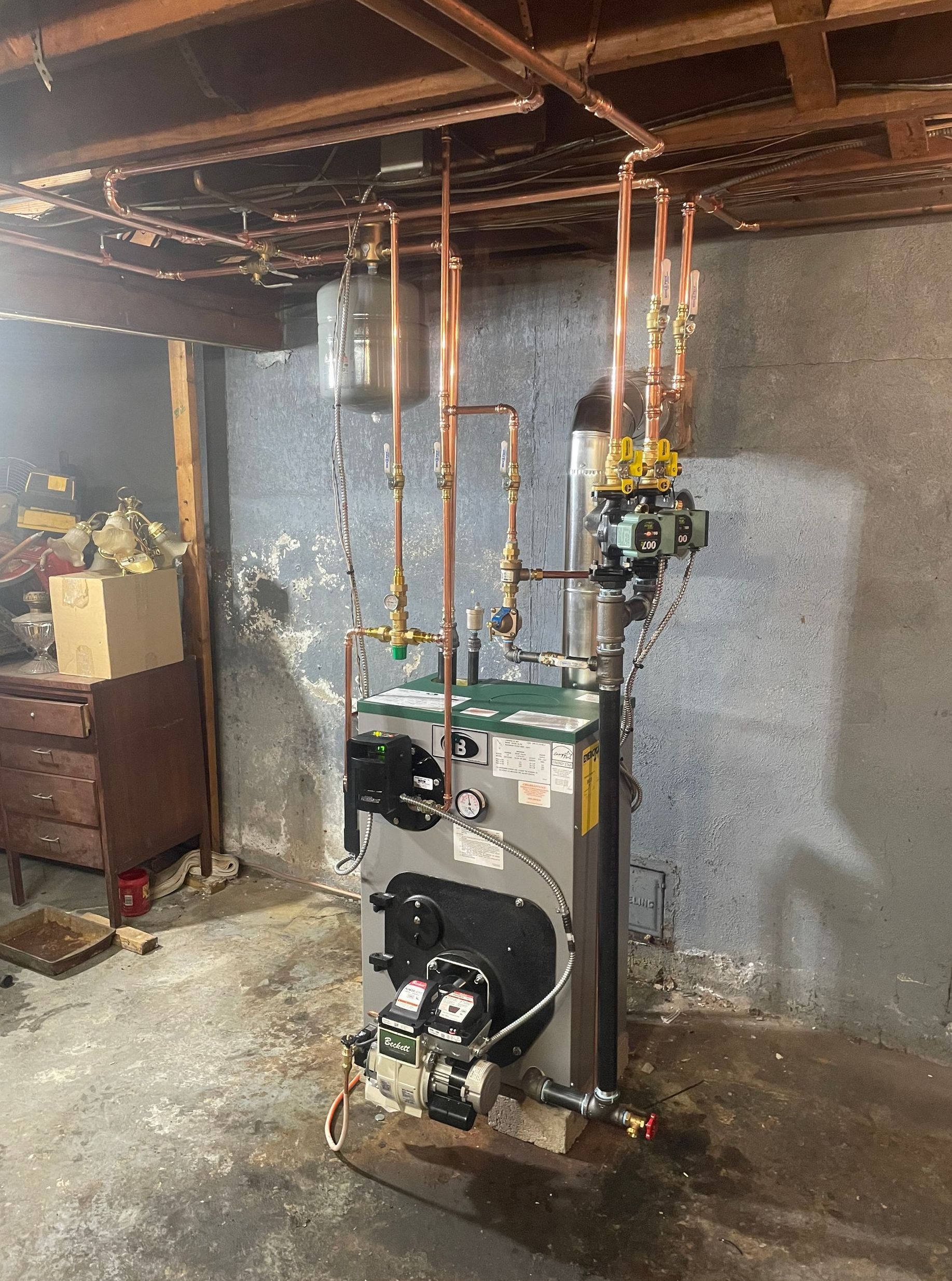 A boiler is sitting in a basement next to a wall.