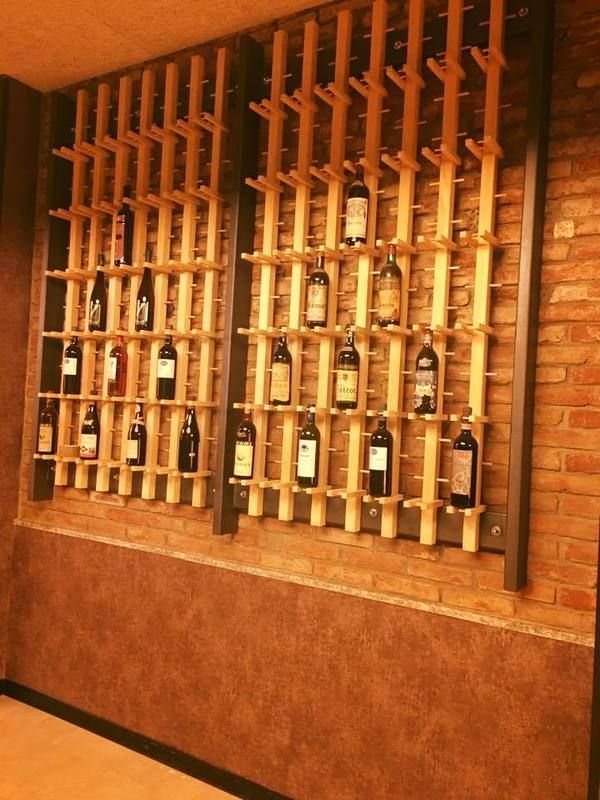Una rastrelliera per vini con diverse bottiglie esposte su listelli di legno contro un muro di mattoni.