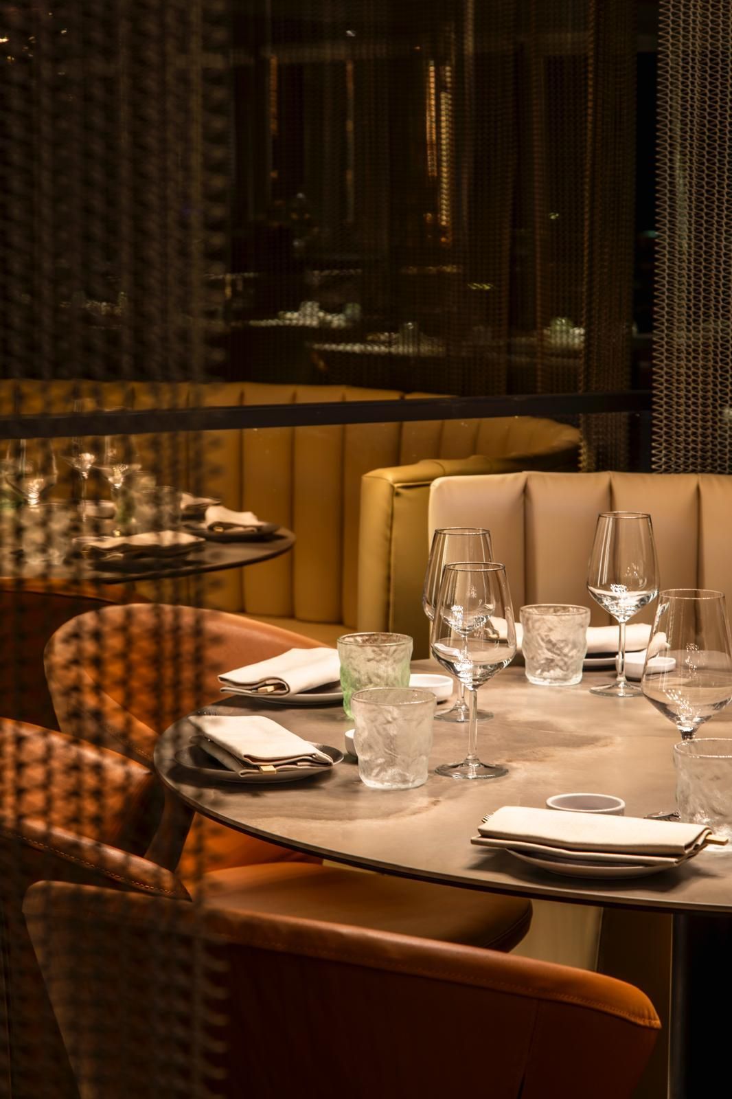 Un ambiente da ristorante con luci soffuse, un tavolo rotondo apparecchiato con bicchieri e tovaglioli piegati
