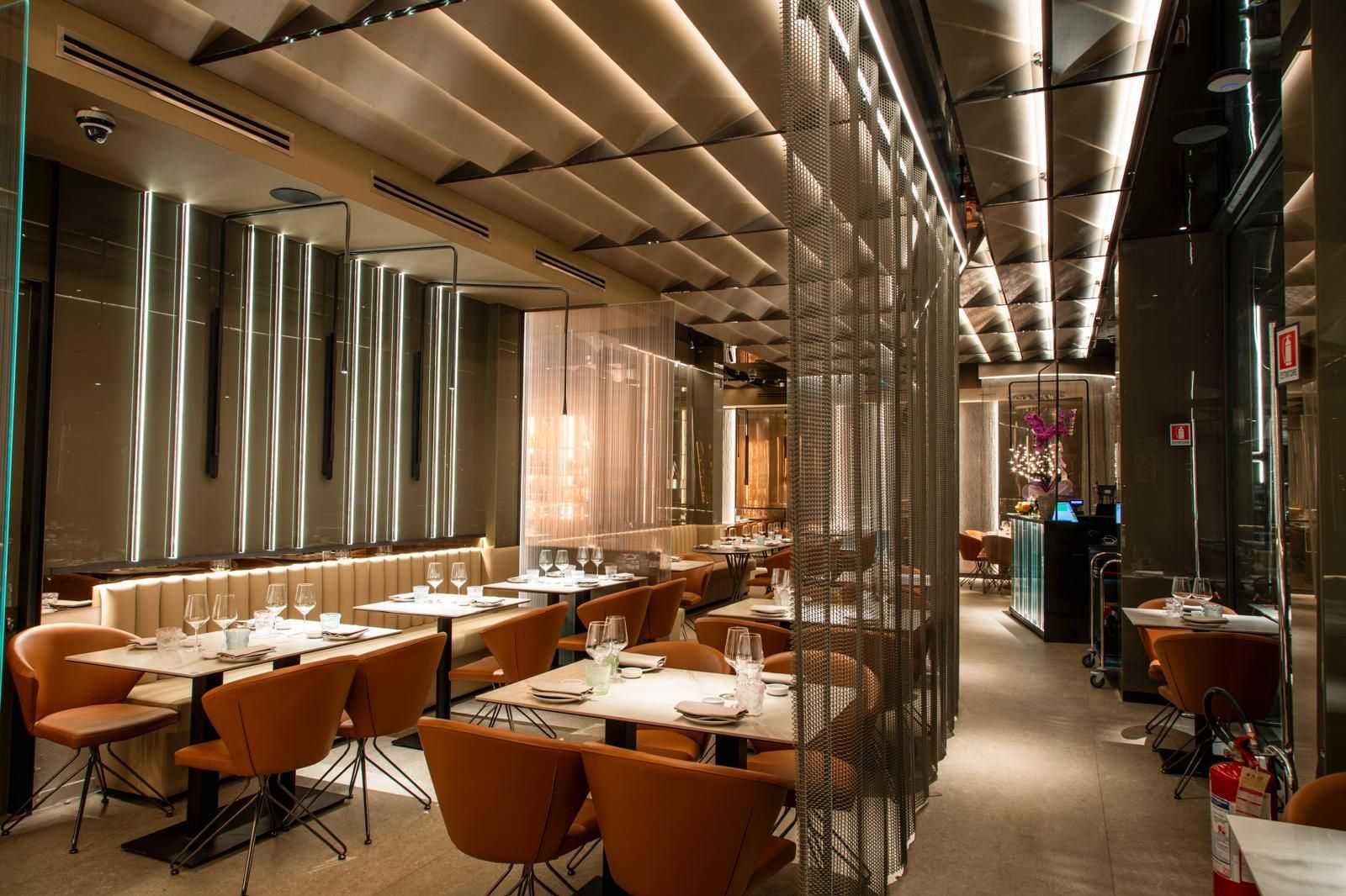Interni di un ristorante di lusso con sedie color cuoio, tavoli in marmo e pannelli luminosi verticali