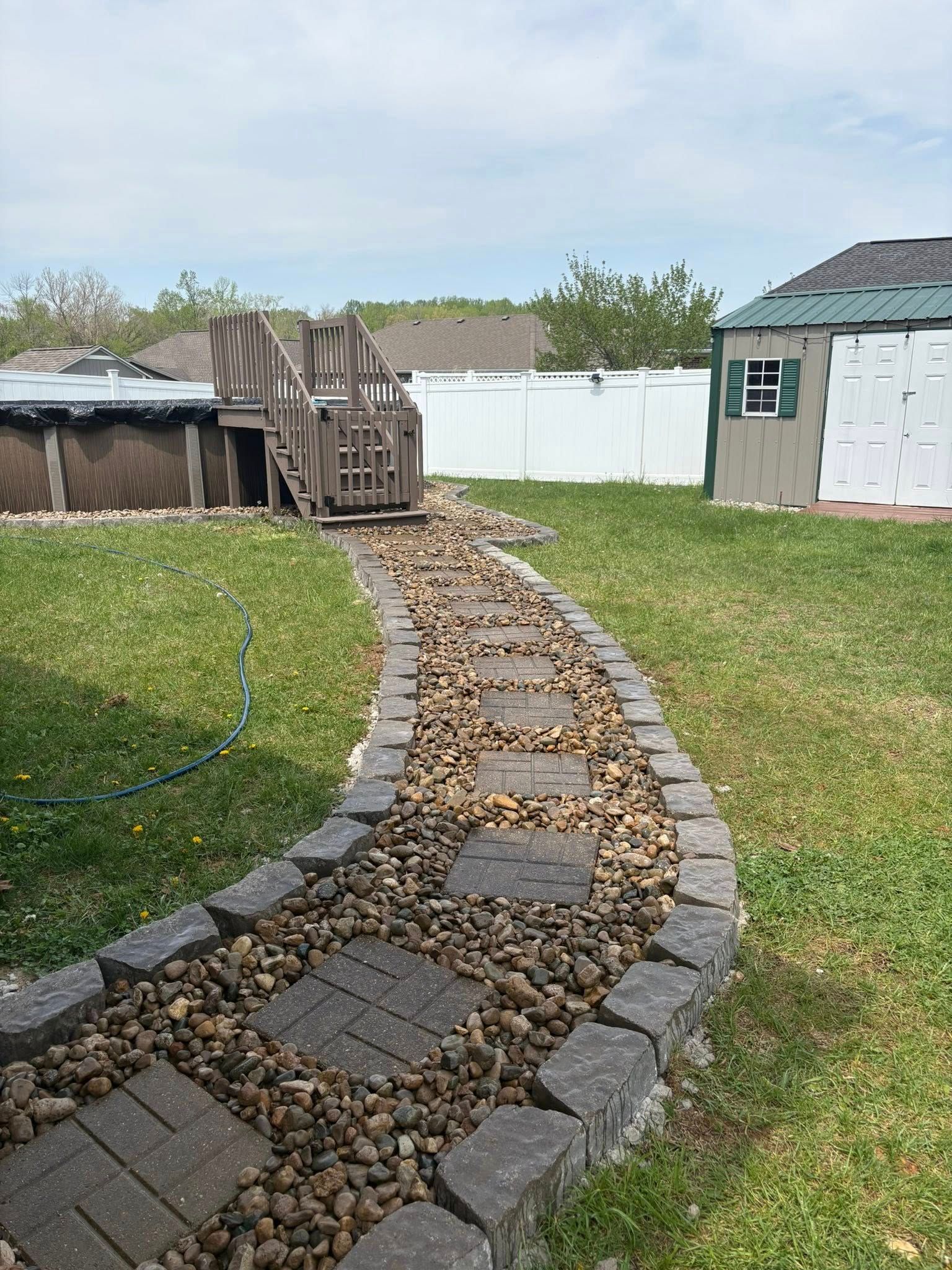 Curved stone-and-pebble garden path leading through a backyard to a white fence and shed.