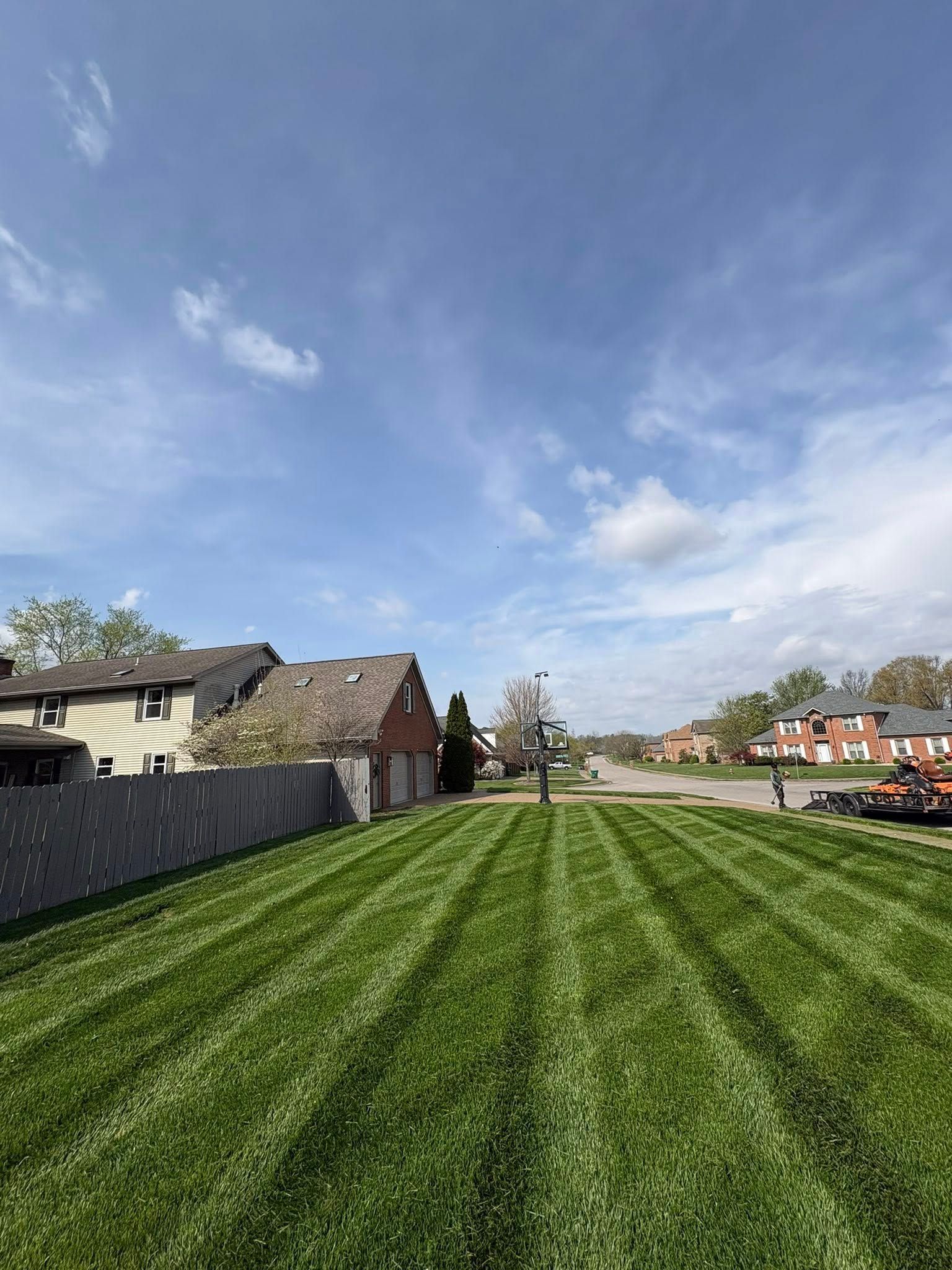 Grassy field with mowing stripes beside houses under a partly cloudy blue sky