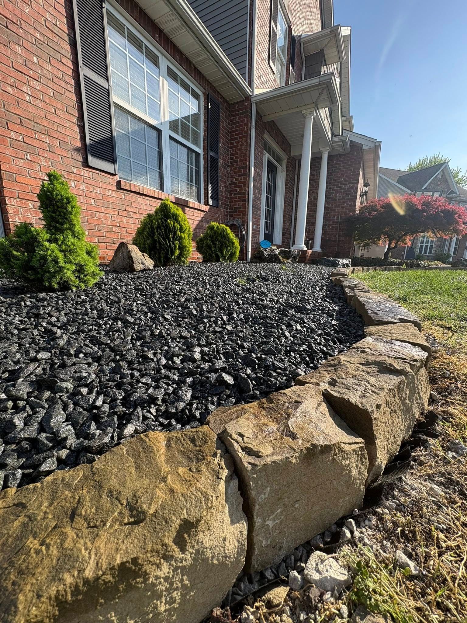 Brick house with black mulch and tan stone retaining wall along a landscaped front path