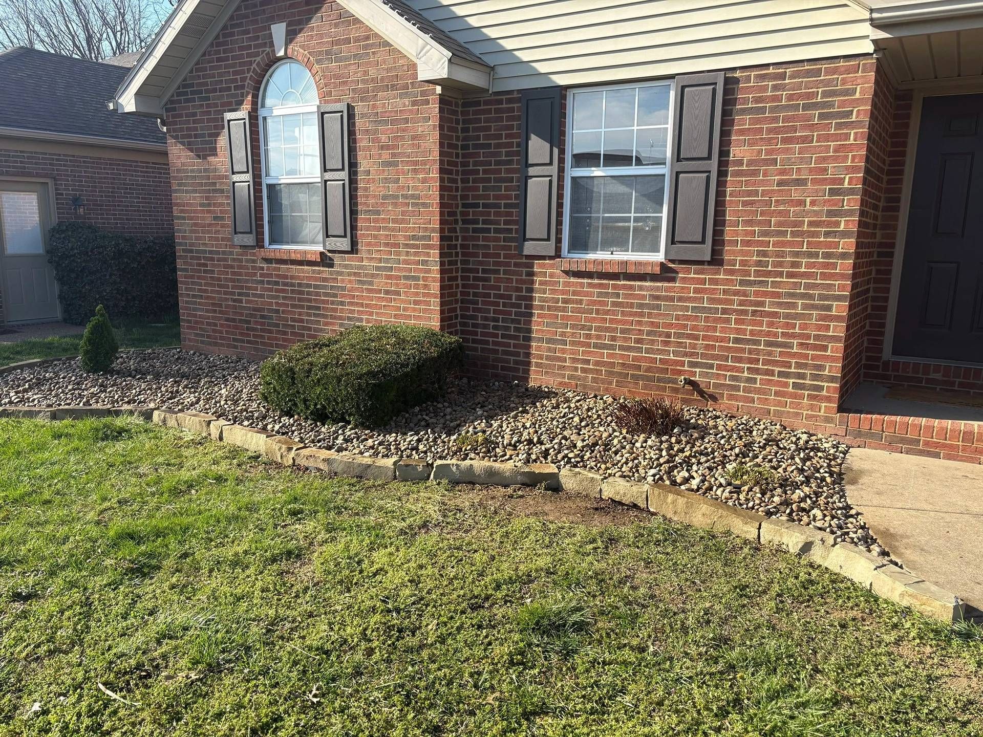 Brick suburban house with arched window, small shrubs, and a sloped front lawn