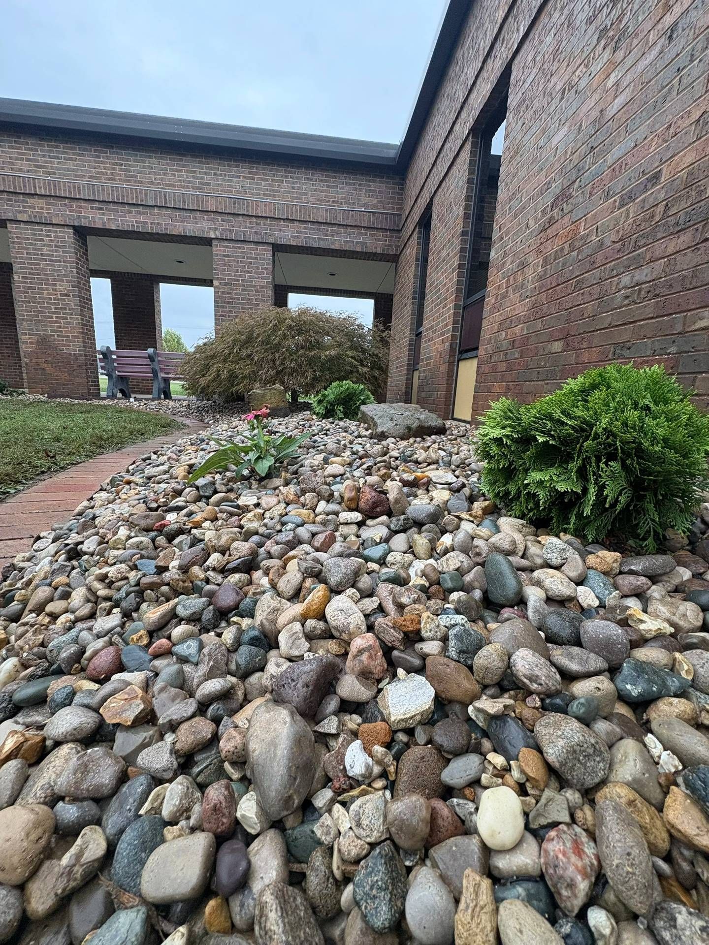 Rock-covered landscaping mound beside a brick building with windows and a small green shrub.