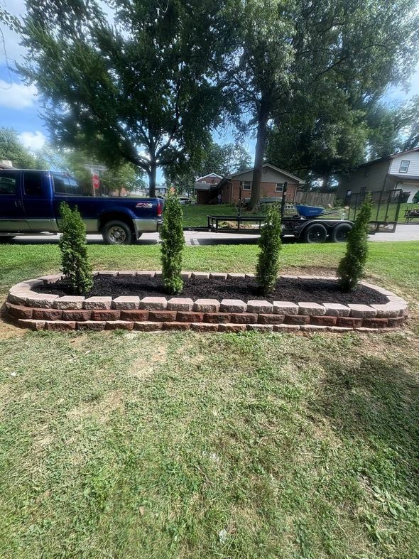 Landscape bed with three trimmed shrubs, brick edging, and mature trees in a front yard