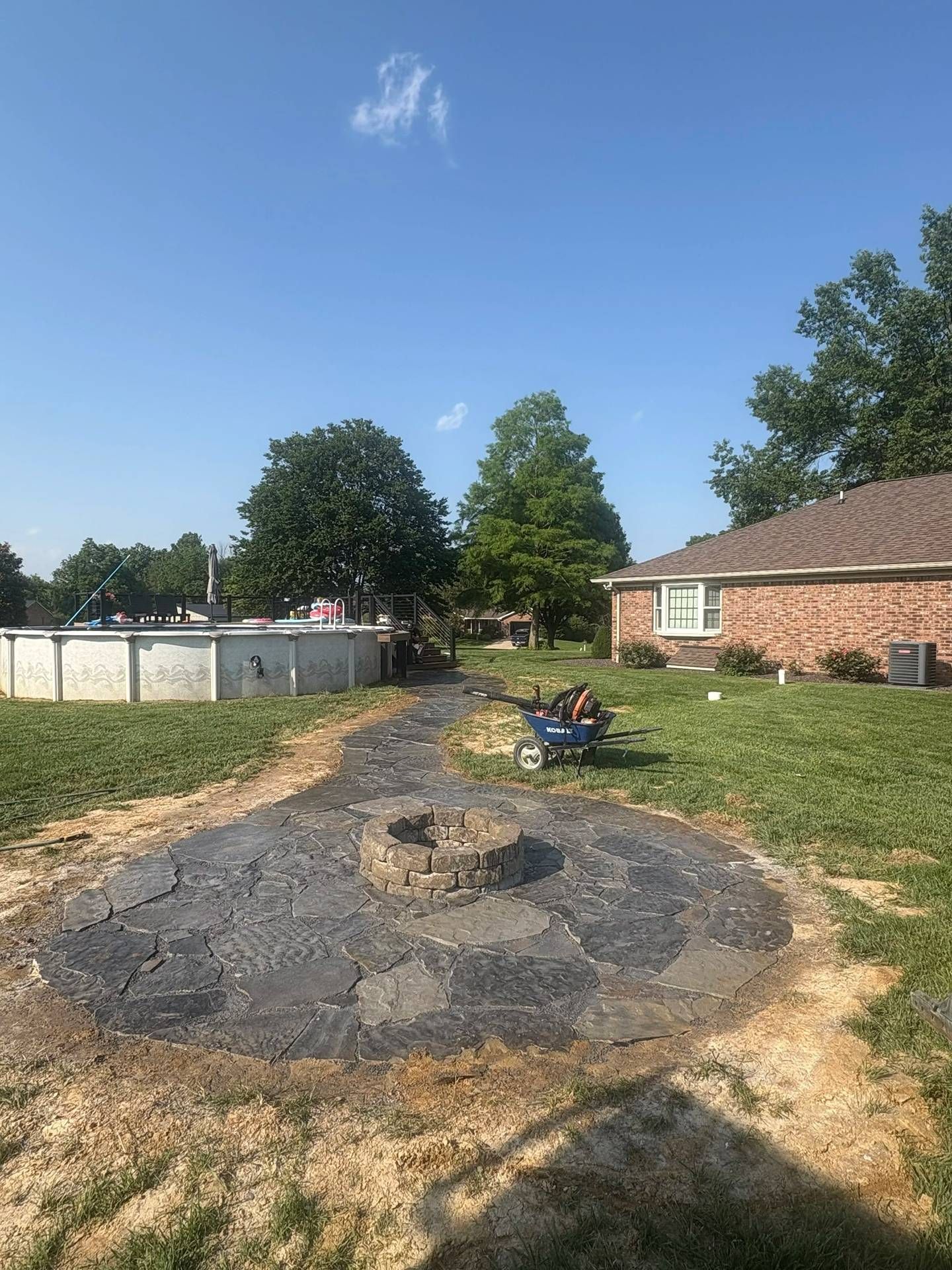 Backyard with a charred fire pit, dirt path, lawn, brick house, and blue sky.