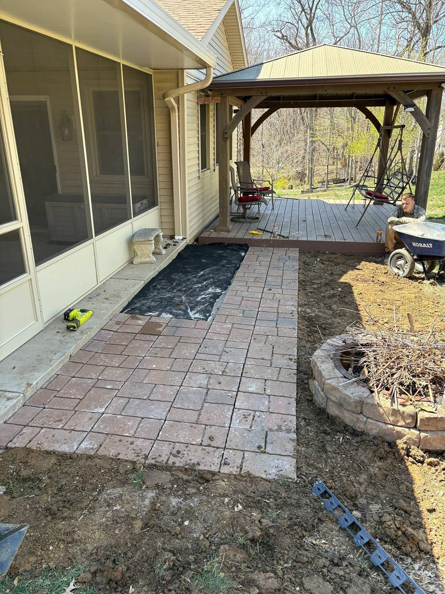 Brick patio path beside screened porch leading to a wooden gazebo and yard in early spring
