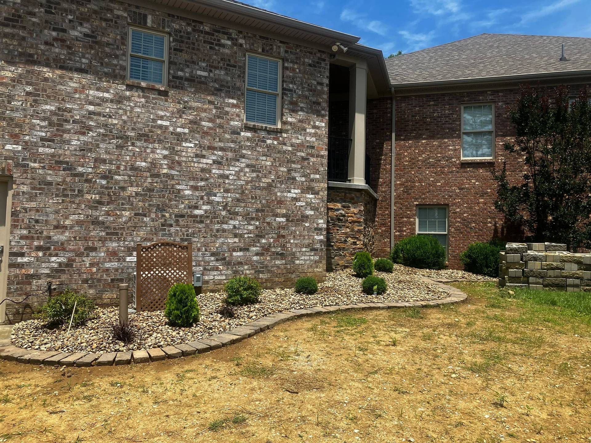Brick house exterior with blue shutters, stone edging, and a dry front lawn