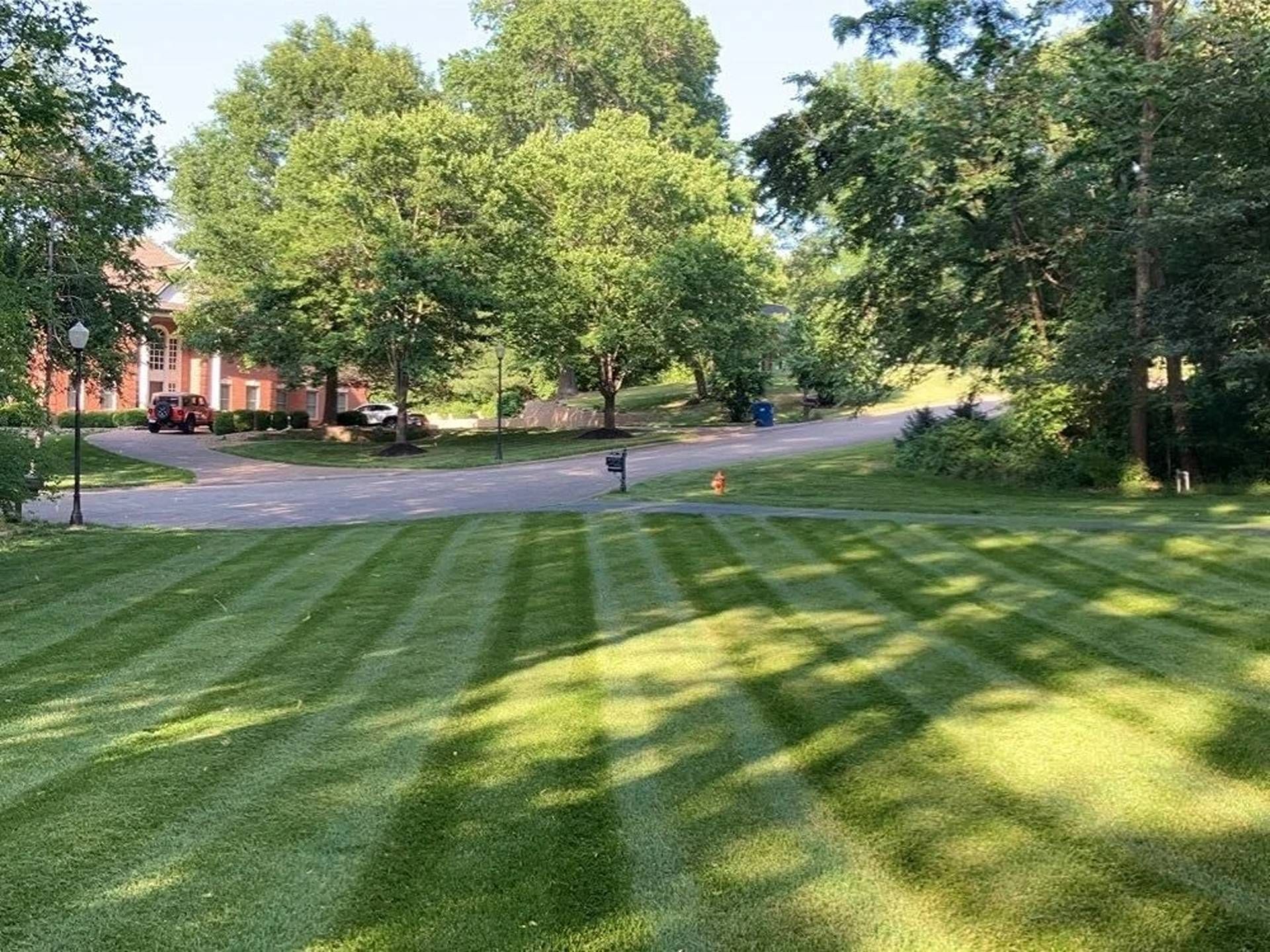 Grassy park lawn with striped mowing patterns, trees, and a red brick building in the background