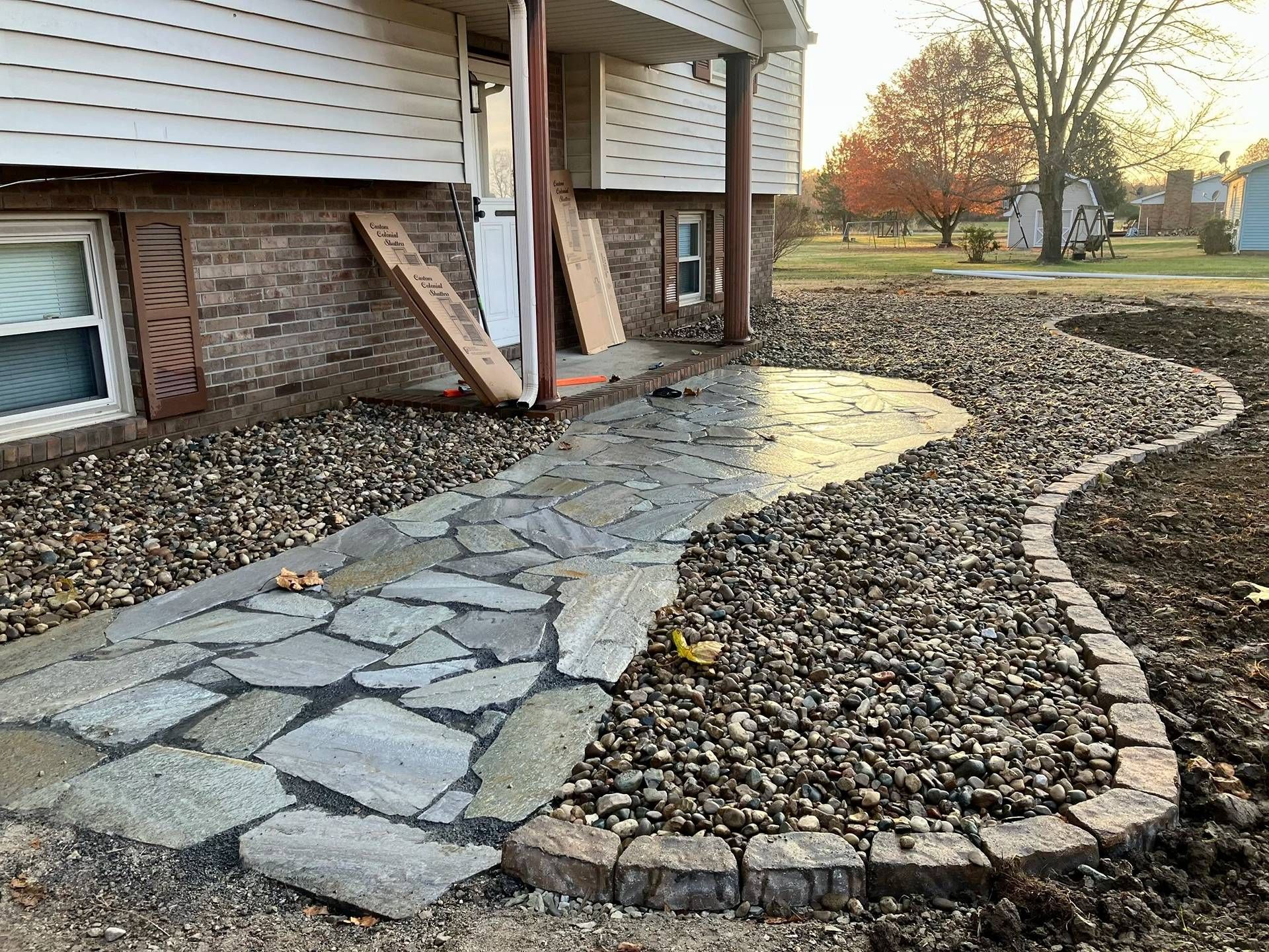 Curved stone walkway beside a brick house with gravel edging and a small yard.