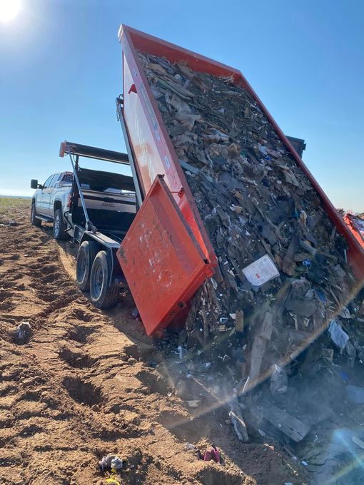 Overturned red truck on a dirt slope with debris spilling out under a clear sky