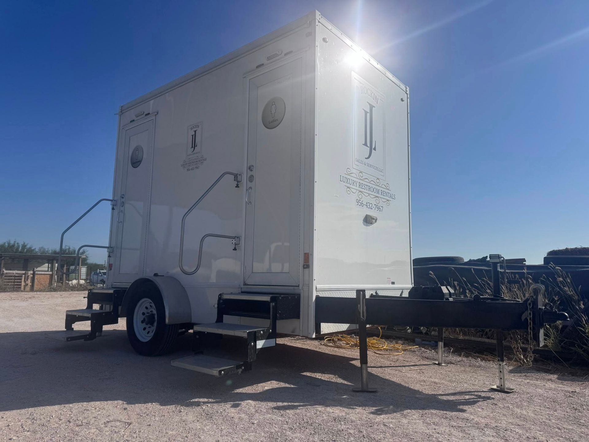 White utility trailer on a gravel lot under a bright blue sky, with sun glare and a hitch at the front