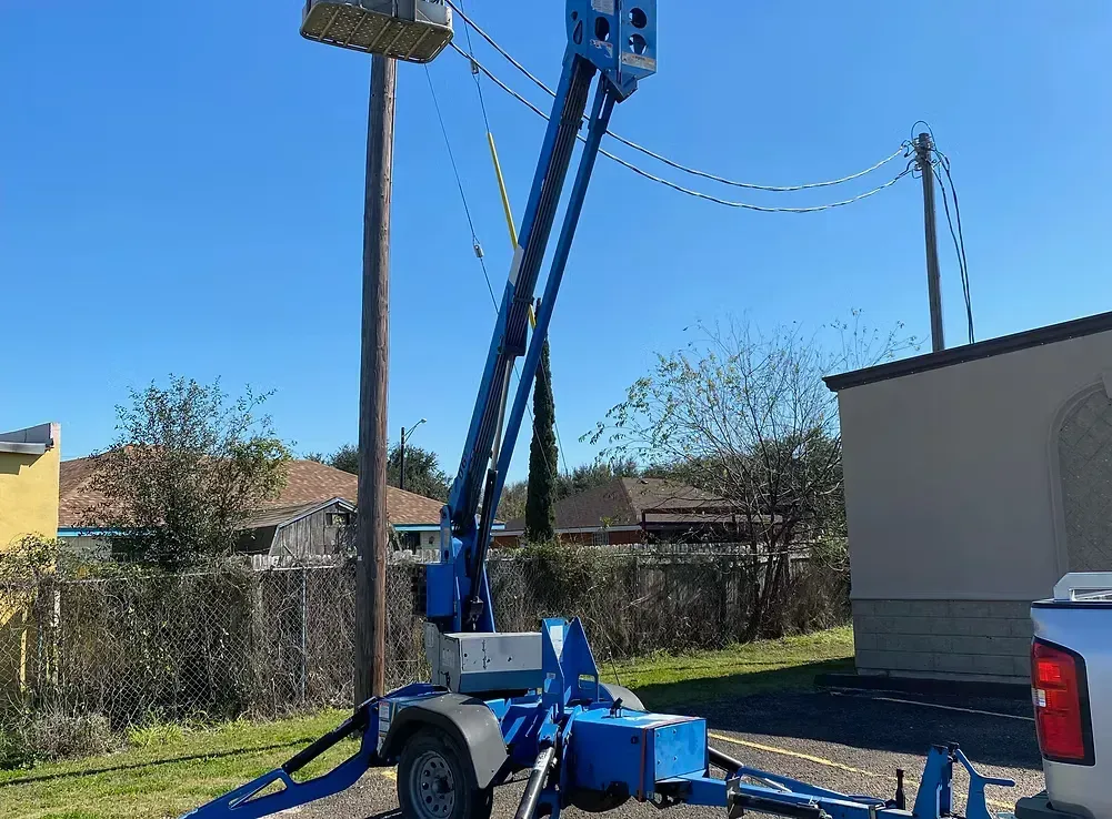 Blue aerial lift truck with raised boom in a residential yard under a clear sky