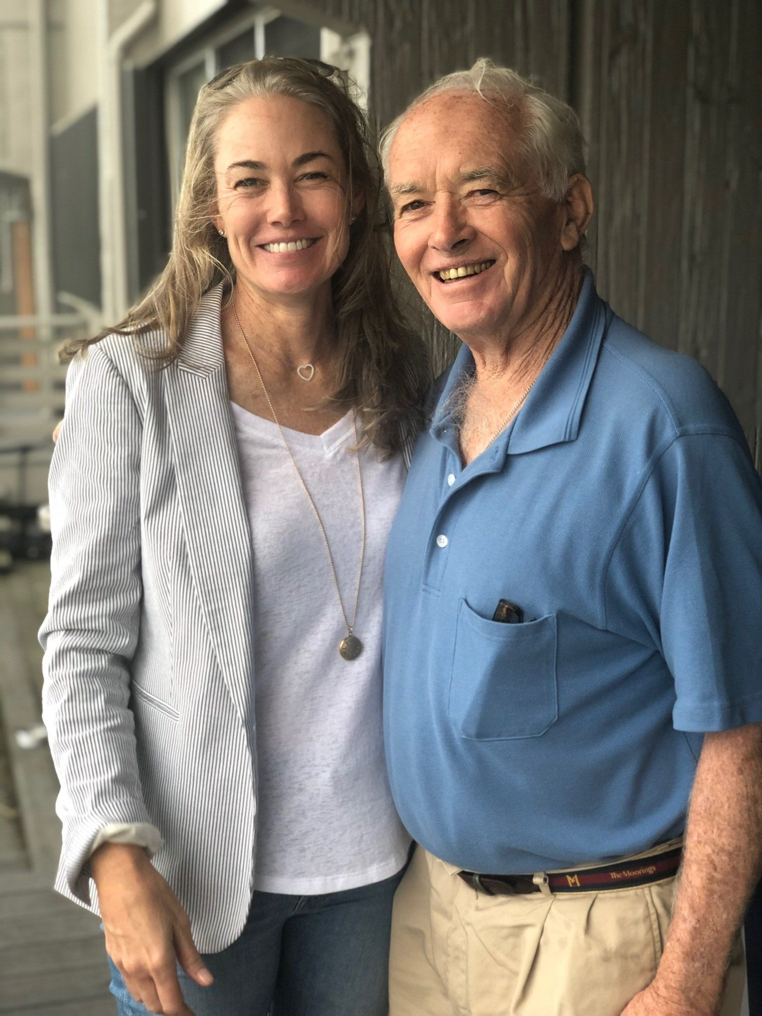 A smiling woman in a striped blazer and a smiling man in a blue polo shirt stand side-by-side posing for a photo.