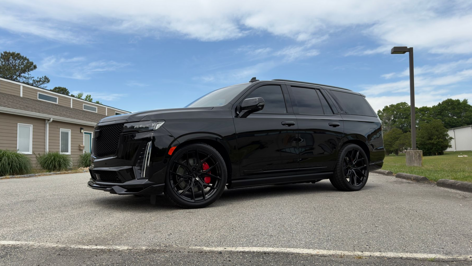 Black SUV with red brake calipers parked on a road near a brick building under a cloudy sky