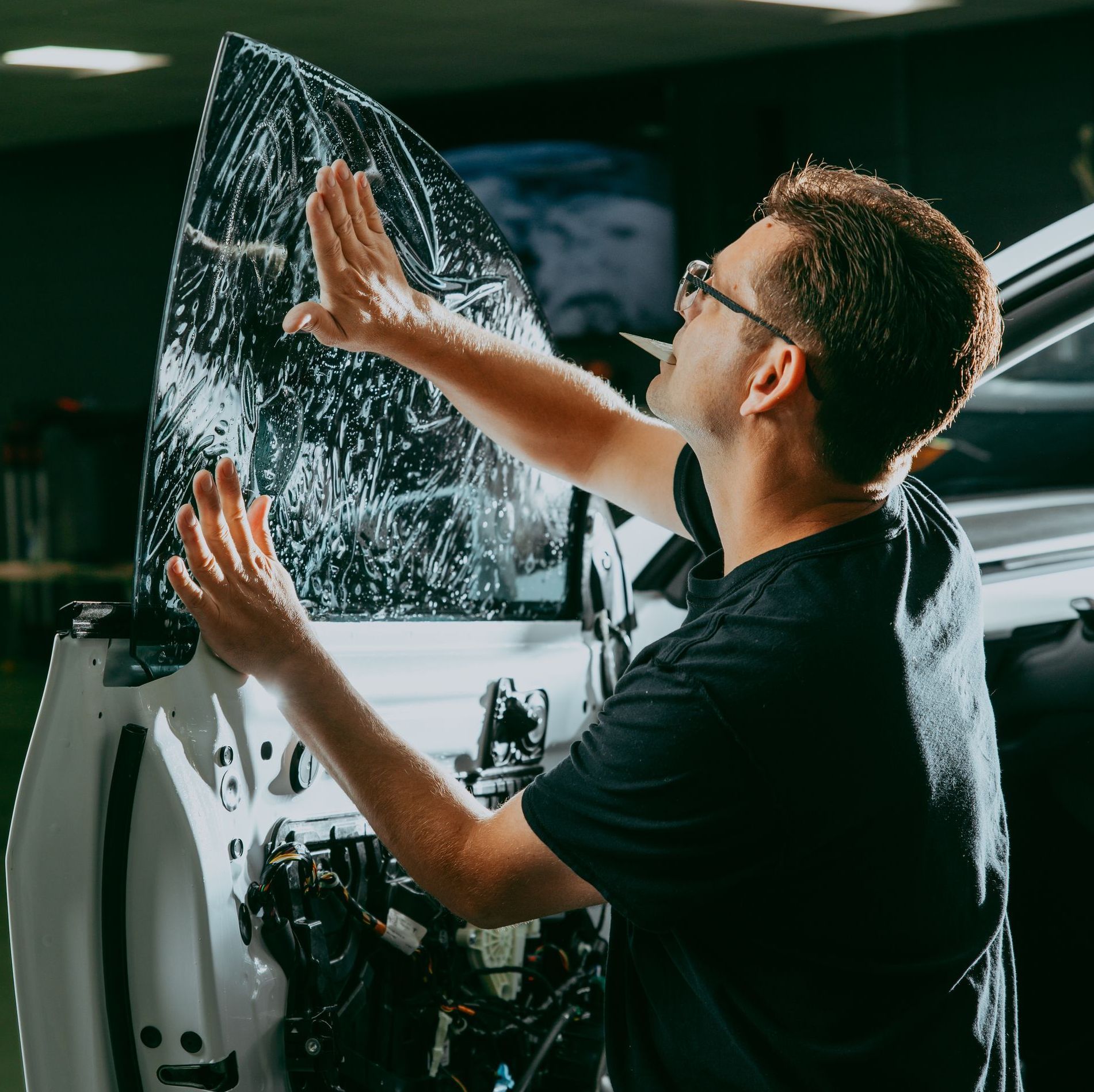A man is applying tinted glass to the window of a car.