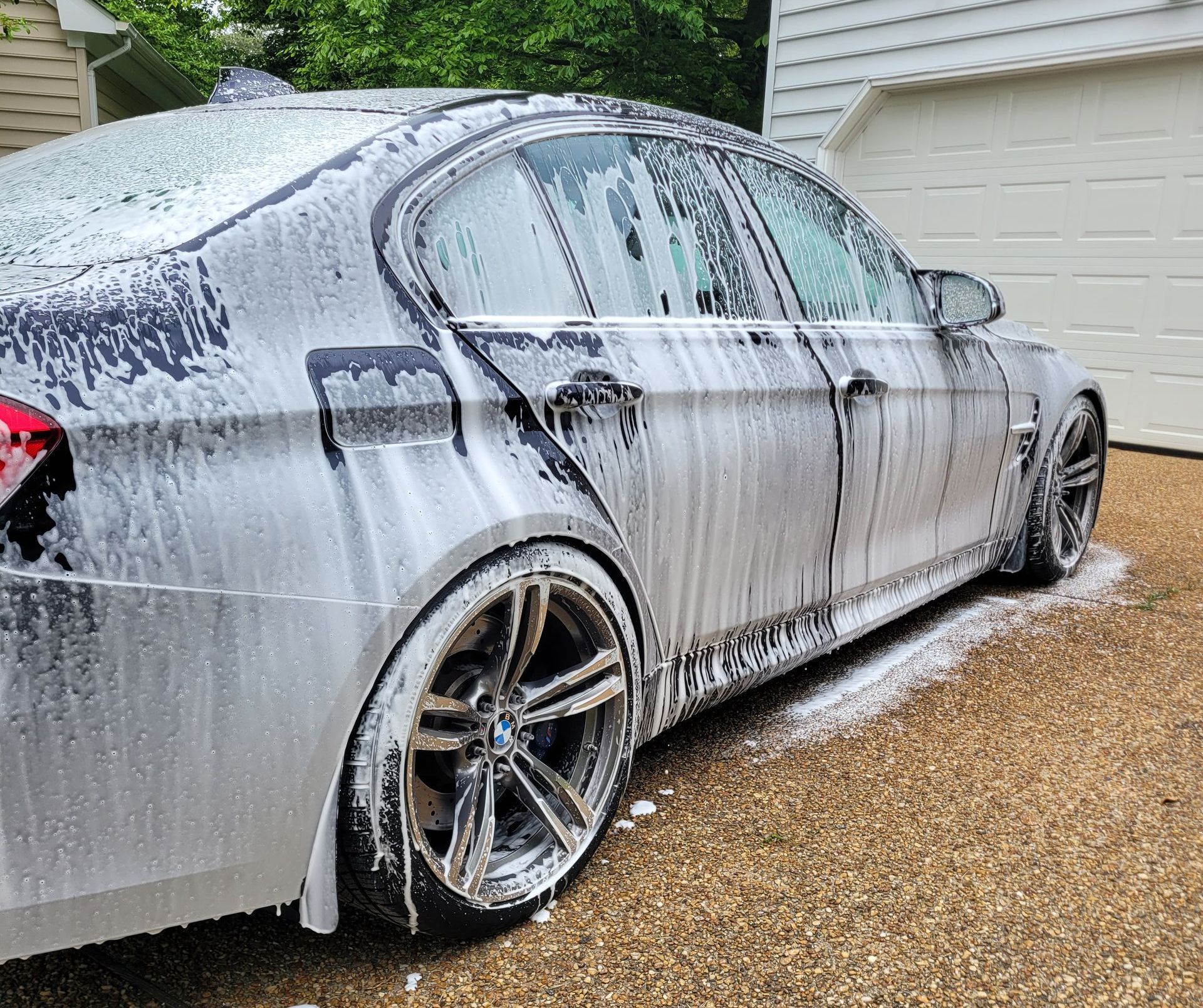 A car is covered in foam in a driveway next to a garage.