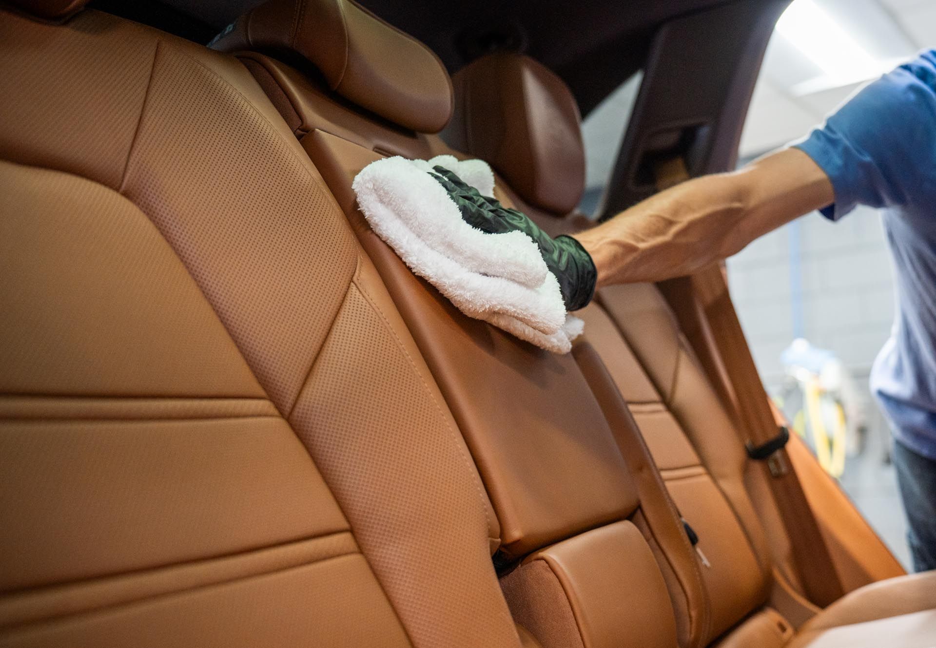 A man is cleaning the back seat of a car with a towel.