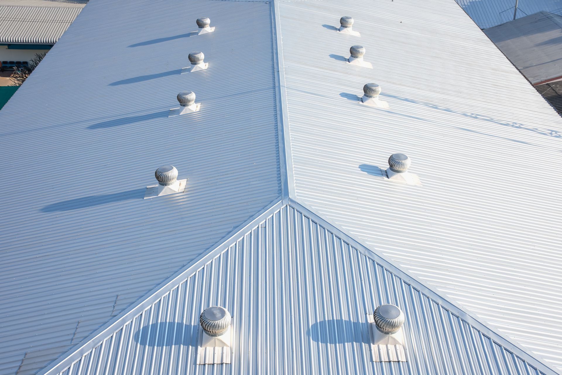 Close up view of a white metal roof with evenly spaced round ventilation caps and ridged panels
