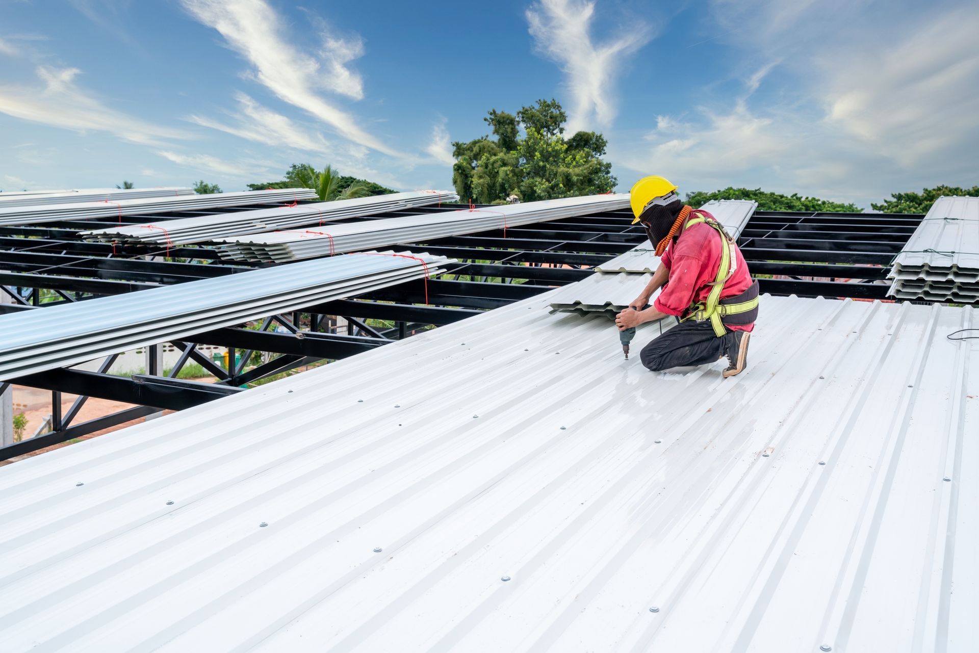 Roof worker installing white metal roofing panels on a commercial building frame.