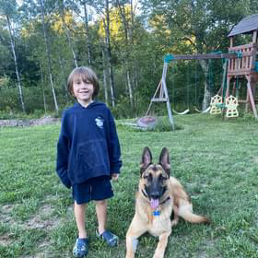 A young boy is standing next to a german shepherd dog in a yard.