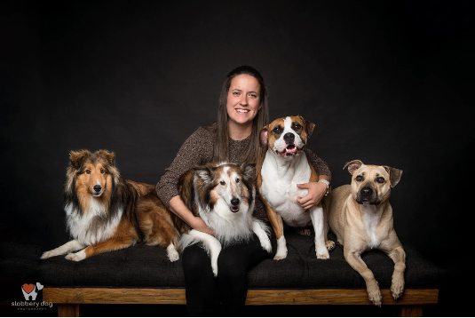 A woman is sitting on a bench with four dogs.