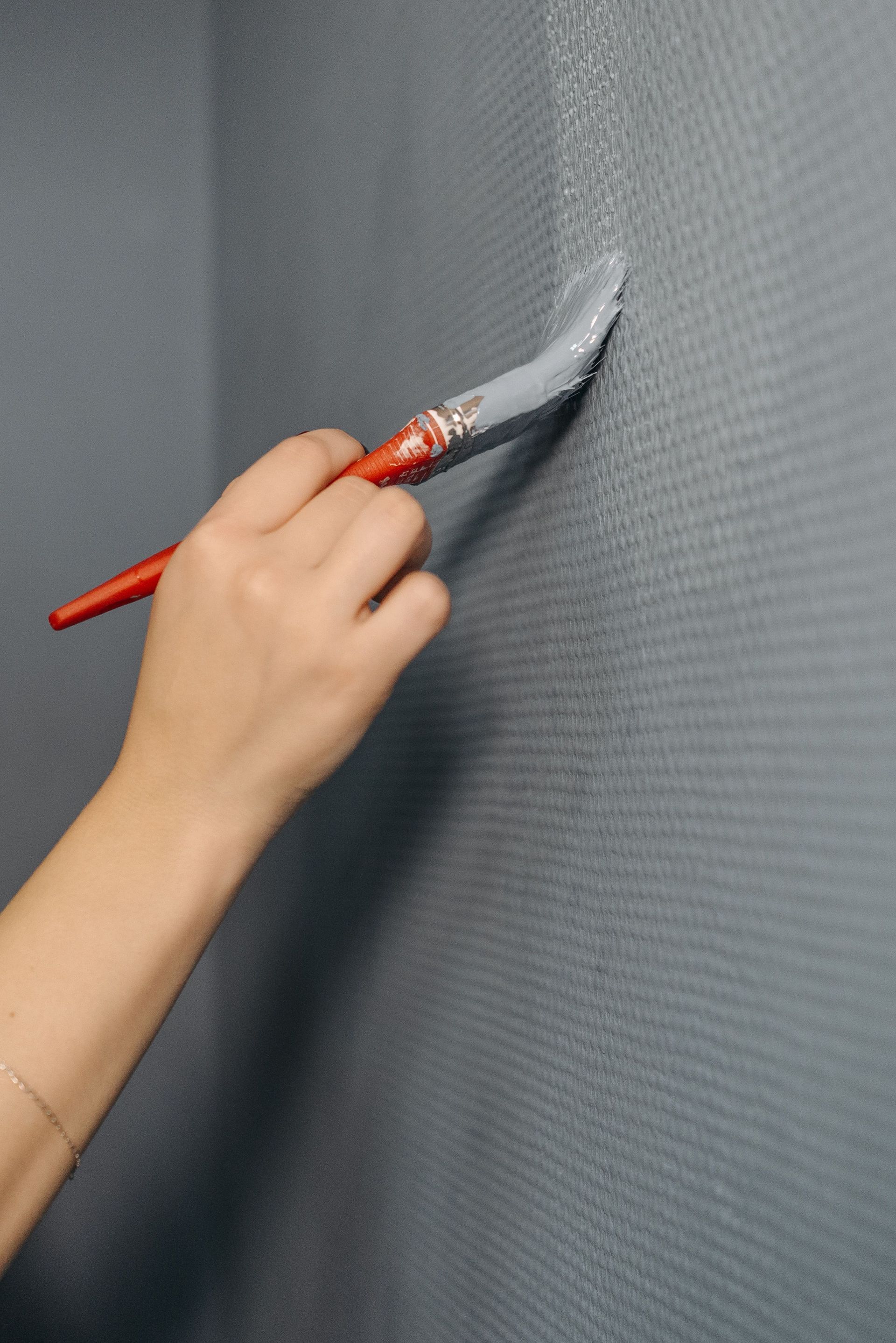 Hand painting a gray wall with a red-handled brush