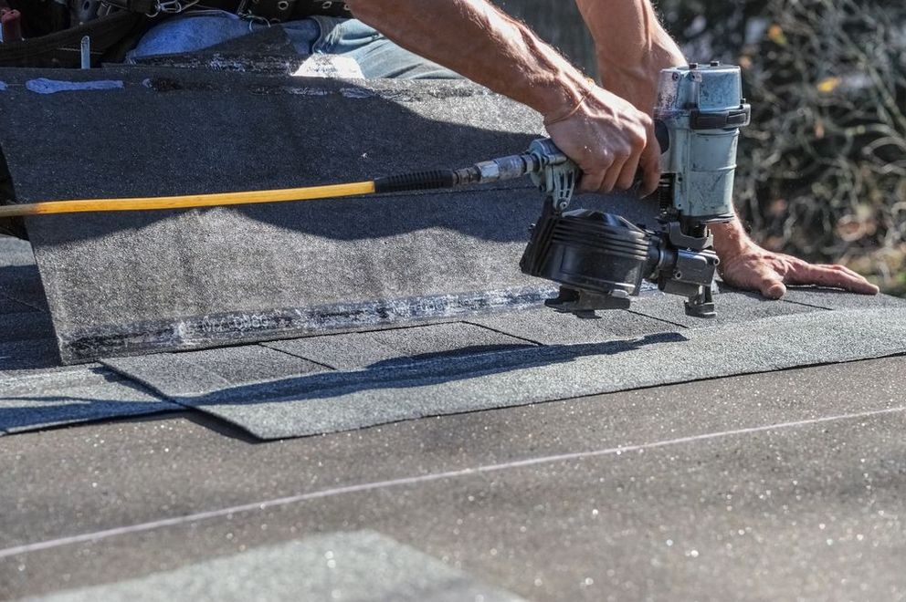 Person using a nail gun to install roofing shingles on a sloped roof