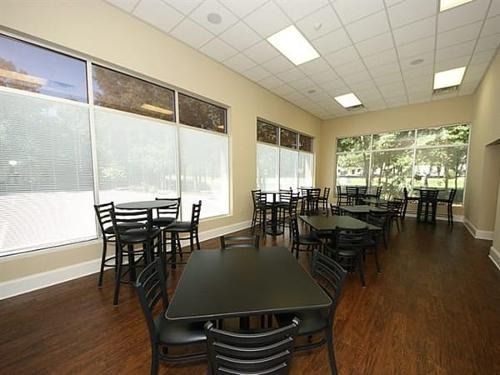 Empty dining room with black tables and chairs, wood floor, large windows, and overhead fluorescent lights