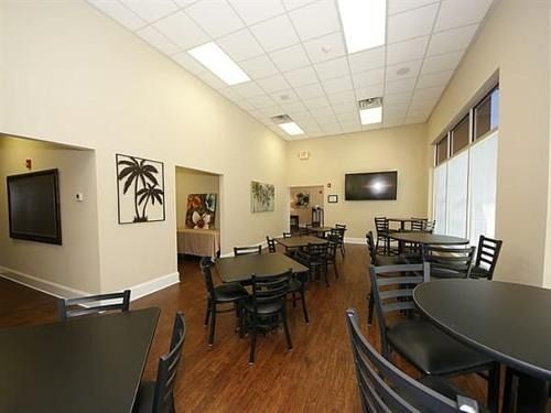 Empty modern café seating area with black tables and chairs, beige walls, and tiled ceiling.