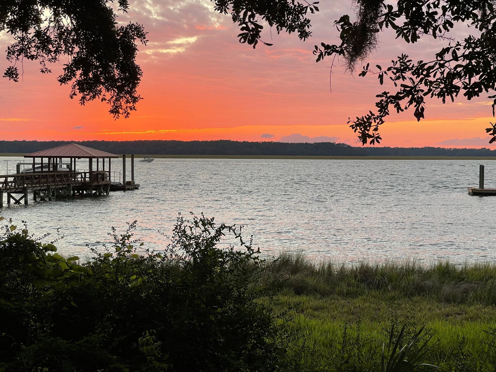 Sunset over a calm lake, with a dock at left and trees framing the shoreline.