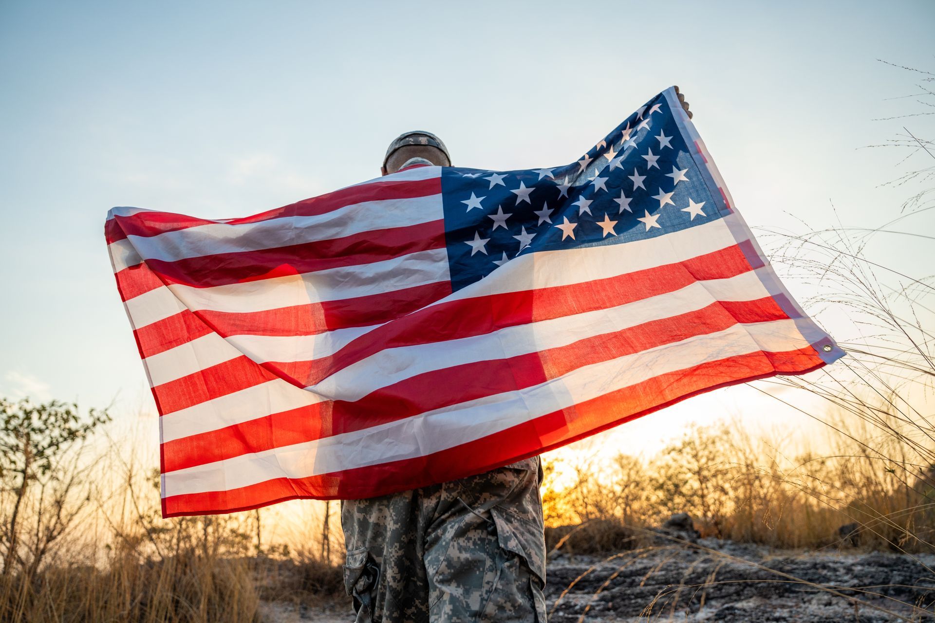 American flag waving outdoors at sunset, held by a person in camouflage