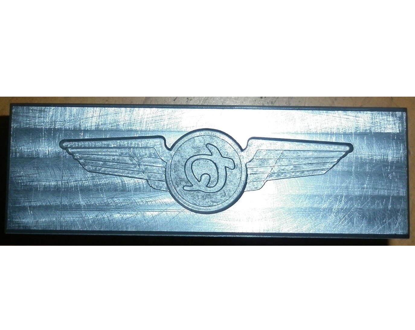 Bloque de metal en relieve con emblema alado que presenta un símbolo omega.