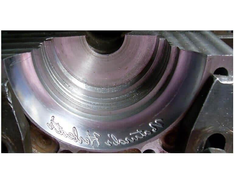 Primer plano de un componente metálico mecanizado con un hueco semicircular y texto grabado.