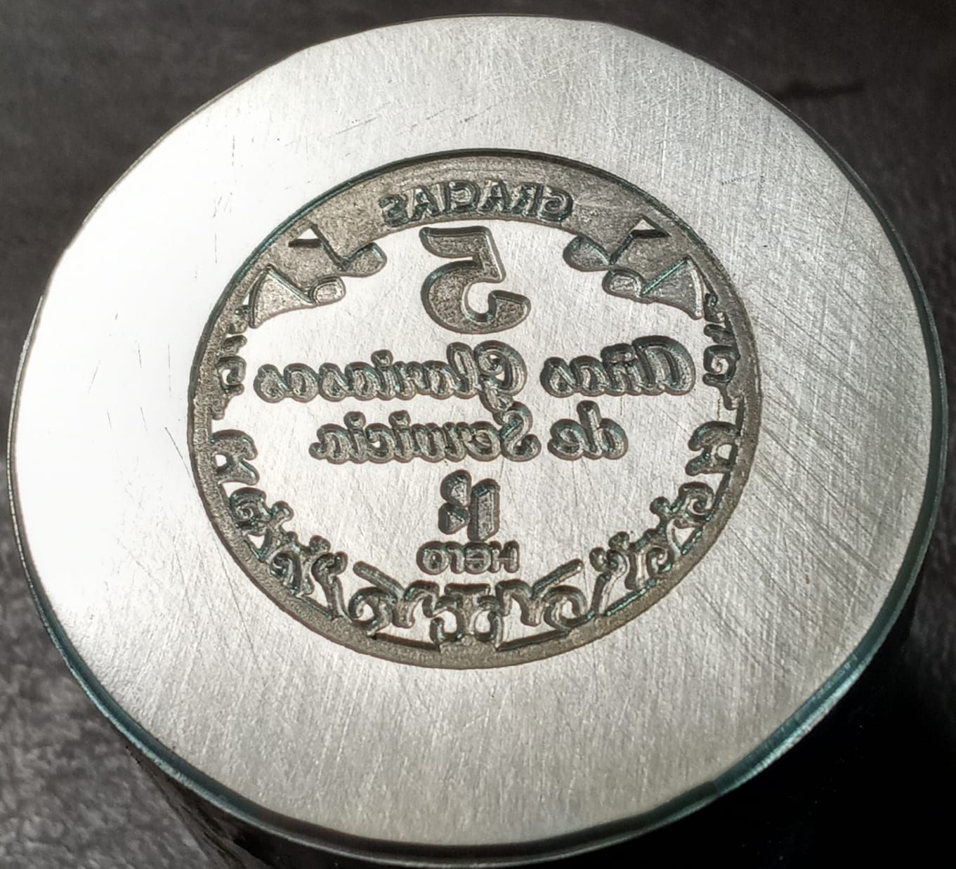 Un sello de metal con texto en un patrón circular, posiblemente utilizado para marcar.