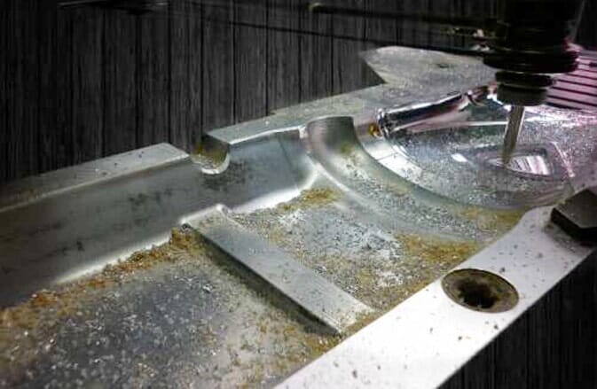 Fresado CNC de una pieza metálica, produciendo virutas en un taller.