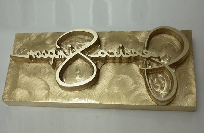 Placa de metal de color dorado con texto estilizado grabado 