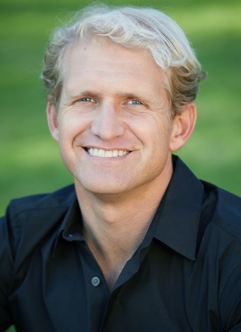 Smiling man in a black shirt against a blurred green outdoor background