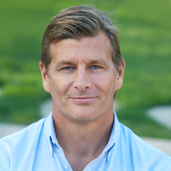 Portrait of a man in a light blue shirt outdoors with a blurred green background