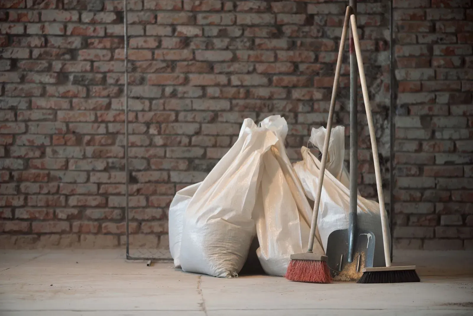 Trash bags and cleaning tools leaned against a brick wall in an empty room.