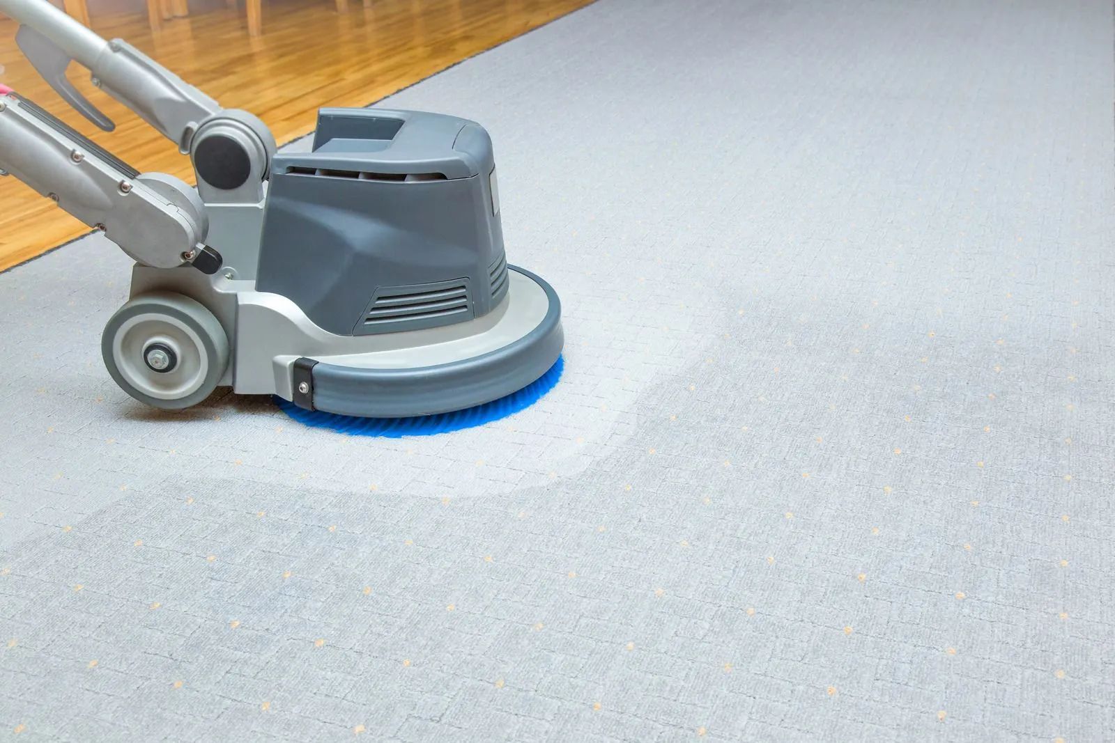 A machine is cleaning a carpet on a wooden floor.