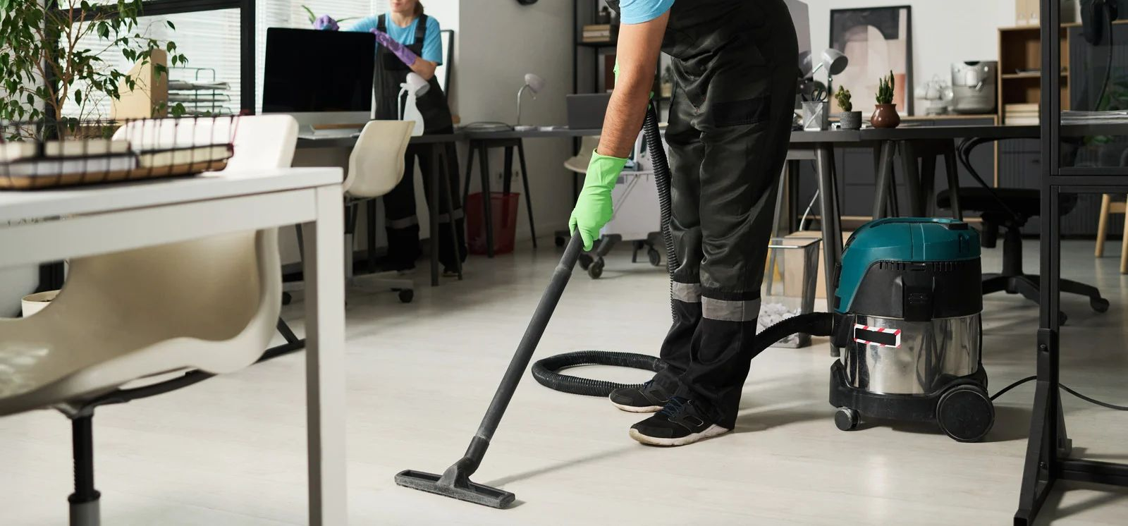 Janitor vacuuming a bright office floor beside cleaning equipment and desks