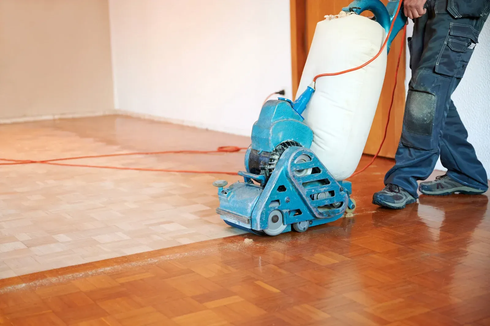 Person using a floor sander on a hardwood floor, removing old finish.