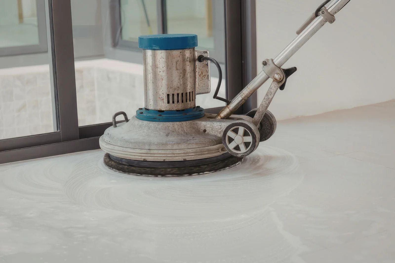 Floor buffer polishing a white surface indoors, with a person’s hands on the handle.