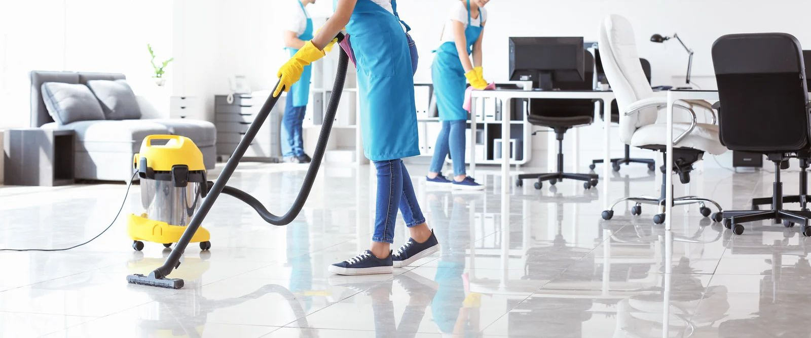 Cleaning staff vacuuming a bright modern office floor with desks and chairs in the background