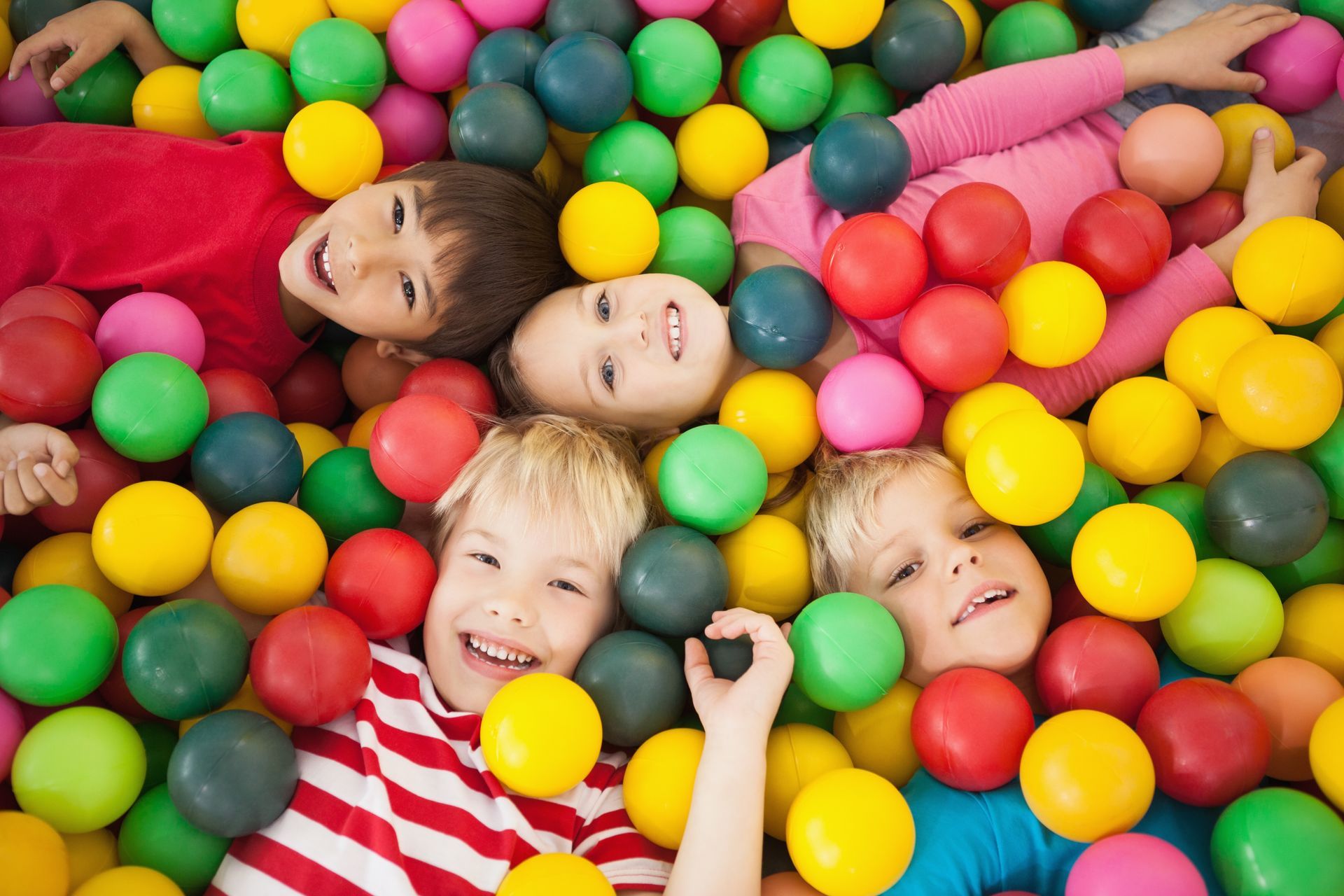 Children laughing in a colorful ball pit, surrounded by bright plastic balls