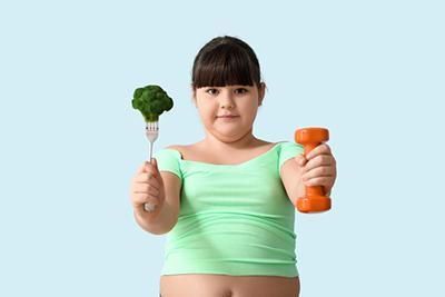 A young girl is holding a fork and a dumbbell.